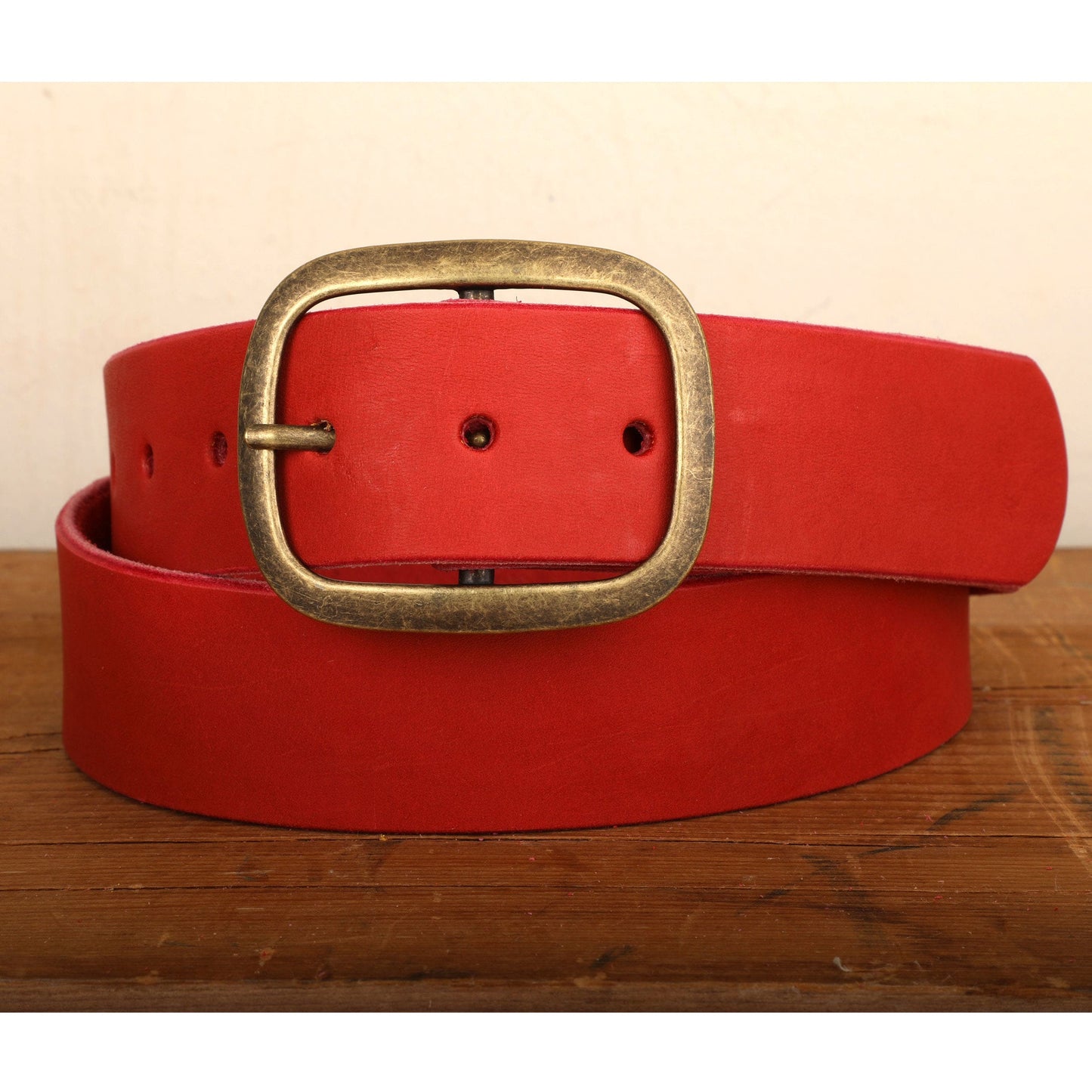 a red belt with a gold buckle on a wooden table