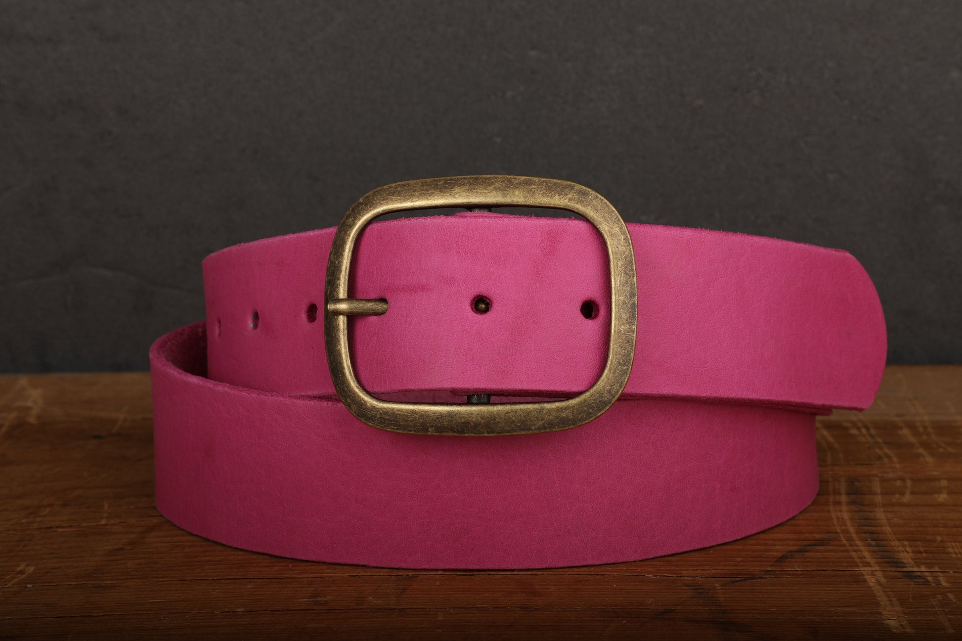 a pink belt with a gold buckle on a wooden table